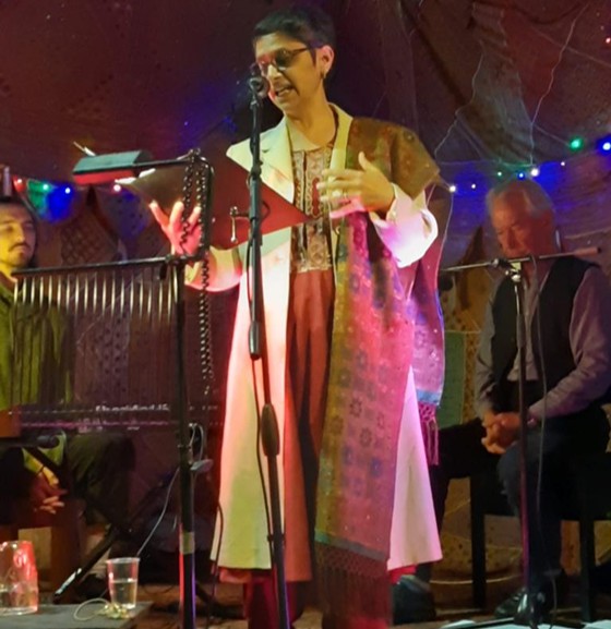 Razia dressed in a colourful robe, standing in front of a microphone delivering a speech